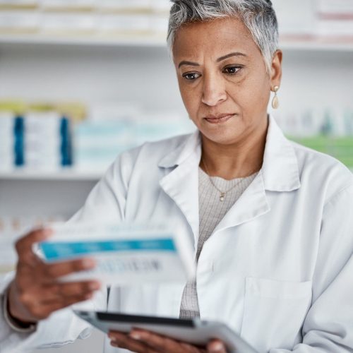 Pharmacist woman, tablet and reading box for information, stock or wellness in store with focus. Senior pharma expert, digital tech and stock in pharmacy for medicine, health or online help in Mumbai.