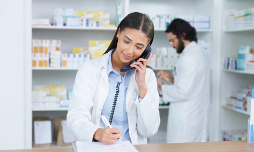 Pharmacist woman answering the telephone and giving advice to customer on flu shot treatment options in pharmacy. Chemist assisting remote client by checking medicine stock on their computer database.