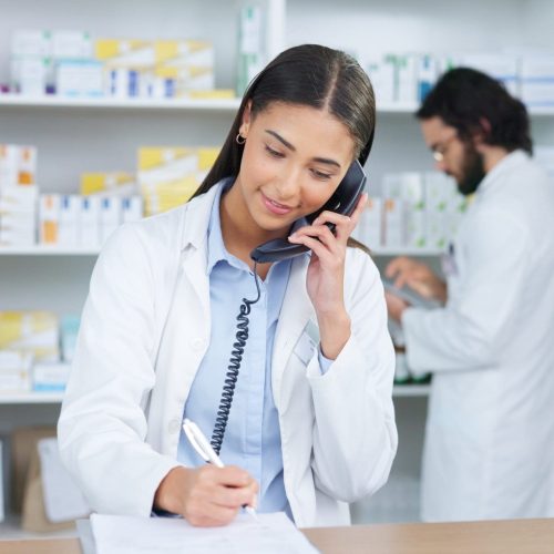 Pharmacist woman answering the telephone and giving advice to customer on flu shot treatment options in pharmacy. Chemist assisting remote client by checking medicine stock on their computer database.