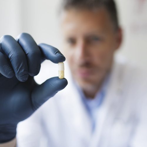 male Doctor with black rubber gloves is holding pills in his hand