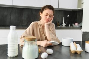 Attractive young cheerful girl baking at the kitchen, making dough, holding recipe book, having ideas.