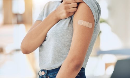 Woman, arm and vaccine with plaster for healthcare, cure or immunity in recovery at home. Closeup of female person with bandaid for covid vaccination, health protection or medical injection at house.